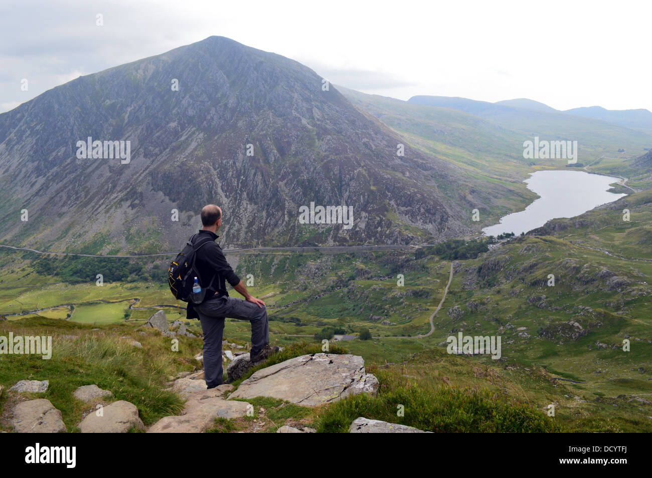 Uomo che guarda in basso vista verso Lyn Ogwen con il Welsh Mountain Pen yr Ole Wen dietro nel Parco Nazionale di Snowdonia Foto Stock