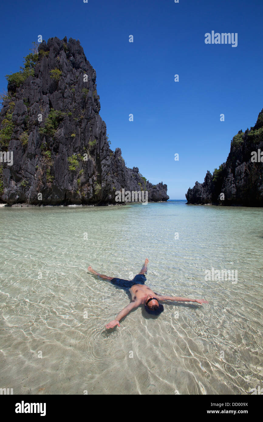 L'uomo galleggianti in acqua chiara della piccola laguna; Miniloc Island, PALAWAN FILIPPINE Foto Stock