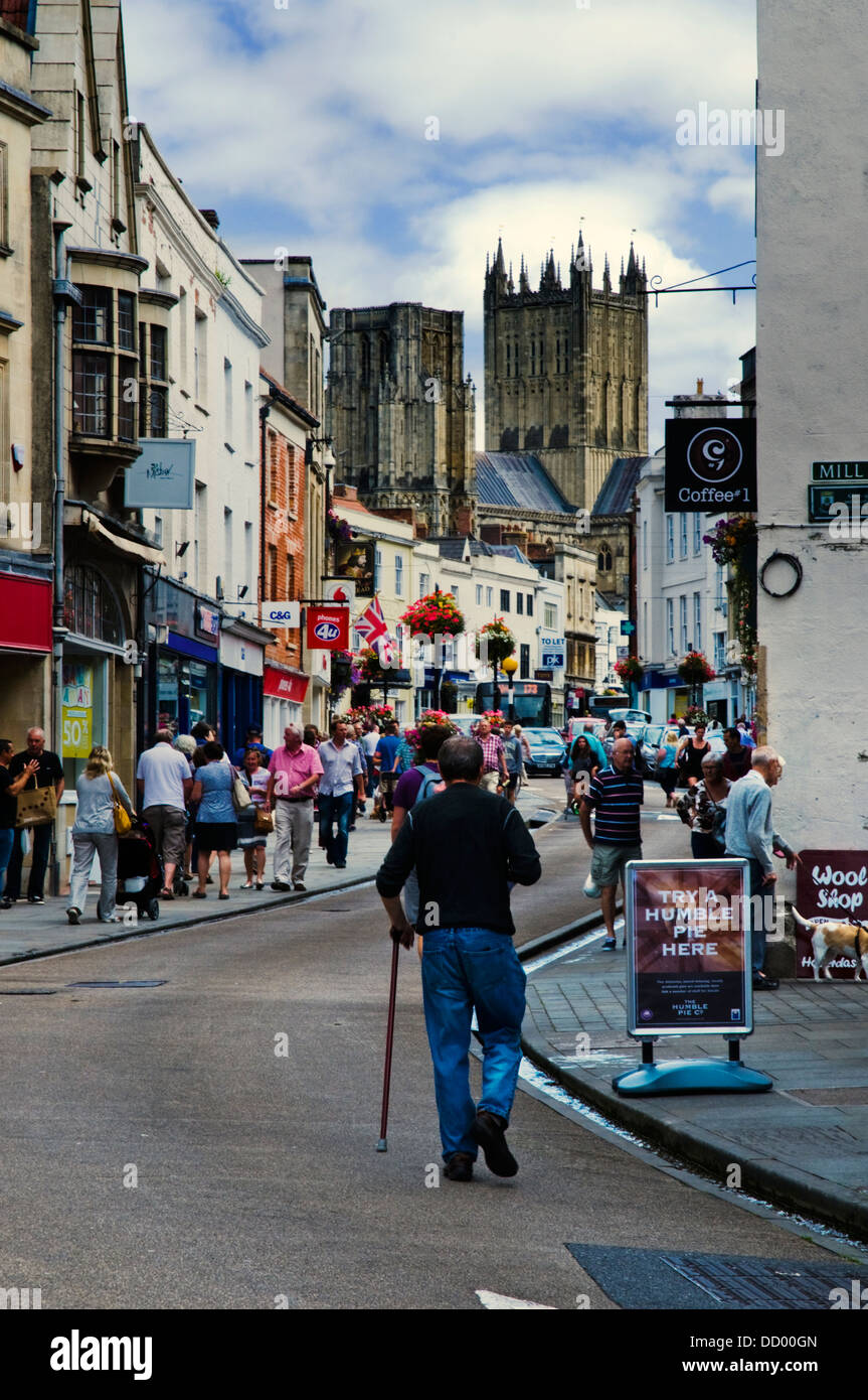 Un uomo con un bastone da passeggio cammina su una strada in pozzi, la più piccola città in Inghilterra verso la cattedrale. Foto Stock