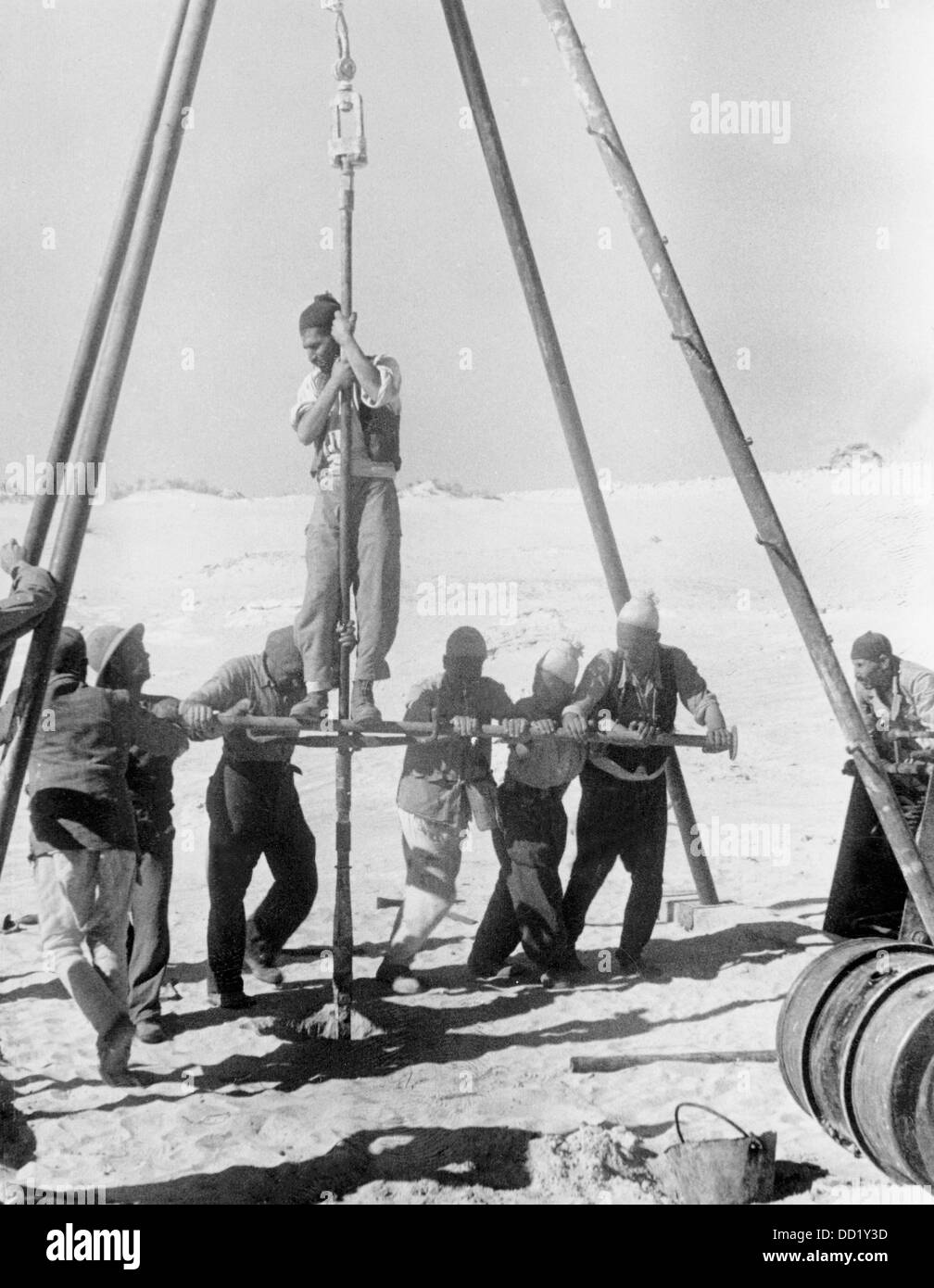 I soldati della Wehrmacht tedesca sono alla ricerca di acqua insieme alla gente del posto nel deserto di Tunesia il 5 maggio 1941, luogo sconosciuto. Propaganda nazista! Sul retro della fotografia: 'Alla ricerca di acqua nel deserto. Un breve rapporto dal davanti dietro il davanti. Un semplice ponteggio porta la punta. La gente del posto aiuta i soldati con il lavoro difficile. Ripetutamente, la perforatrice colpisce la roccia solo pochi metri sotto il suolo, quindi la pietra deve essere scalpellata fuori." (Difetti di qualità dovuti alle condizioni del materiale storico). Fotoarchiv für Zeitgeschichte Foto Stock
