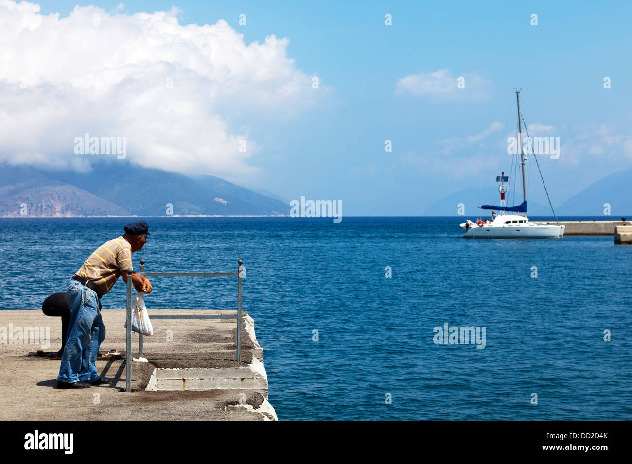 Vecchio Pescatore greco appoggiata sulla barriera che guarda al mare Kefalonia acqua turchese grecia isola Foto Stock