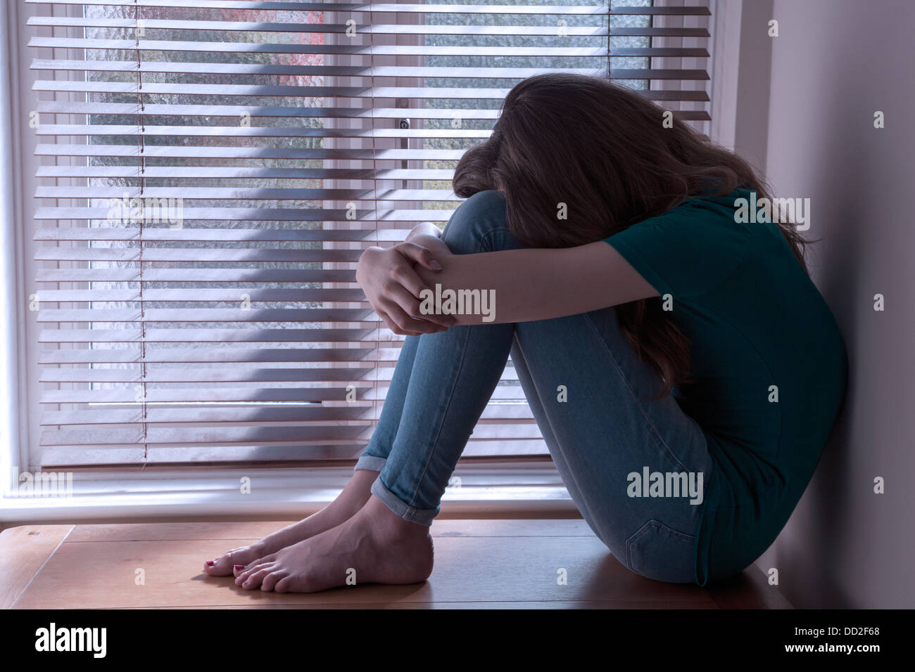 Una ragazza adolescente, faccia in grembo, seduti in una finestra con una luce di colata. Foto Stock