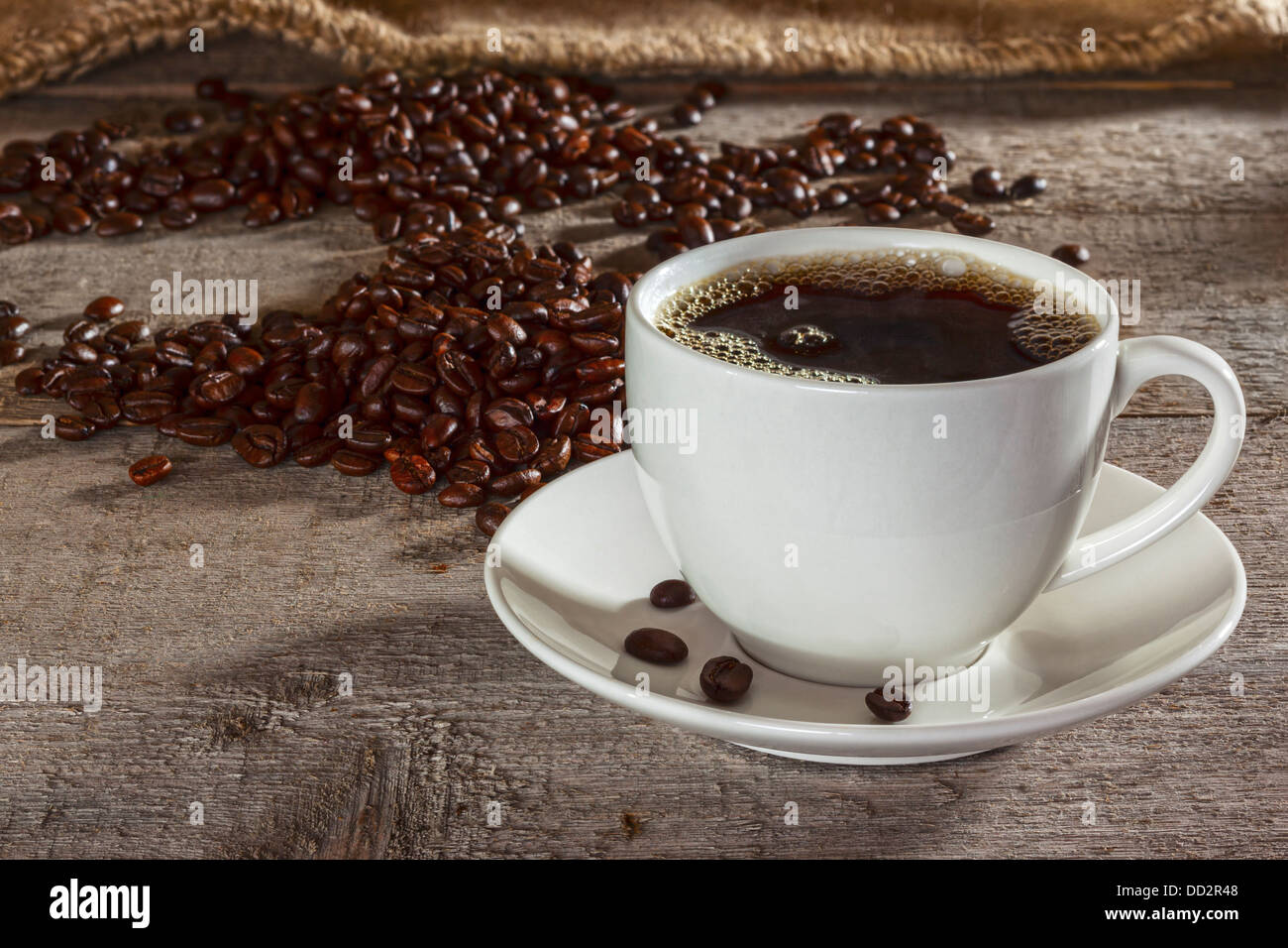 Tazza di caffè e caffè in grani 0n sfondo rustico - tazza da caffè con piattino riempito con caffè espresso, con i chicchi di caffè e tela... Foto Stock