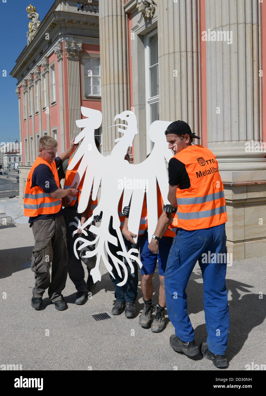 Lavoratori portano il nuovo stemma ufficiale della stato il parlamento del Land di Brandeburgo, l'aquila, in plenar hall del nuovo edificio del parlamento a Potsdam, Germania, 24 agosto 2013. La stilizzata aquila prussiana realizzato in lamiera di acciaio laccata bianco e pesa più di 100 chili. Lo stato europeo verrà aperto nella ricostruita Potsdam City Palace nel gennaio 2013. Foto: Ralf Hirschberger Foto Stock