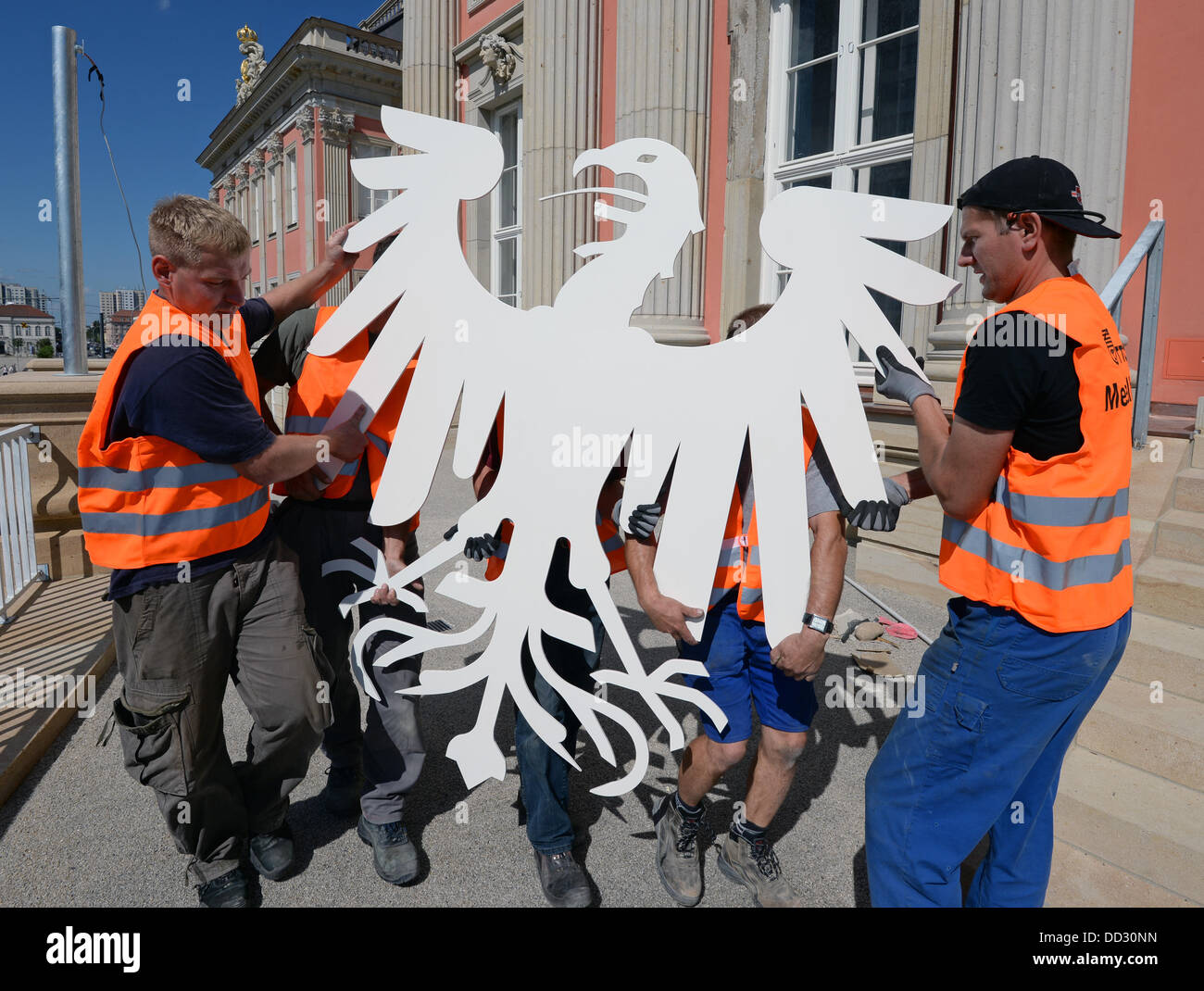 Lavoratori portano il nuovo stemma ufficiale della stato il parlamento del Land di Brandeburgo, l'aquila, in plenar hall del nuovo edificio del parlamento a Potsdam, Germania, 24 agosto 2013. La stilizzata aquila prussiana realizzato in lamiera di acciaio laccata bianco e pesa più di 100 chili. Lo stato europeo verrà aperto nella ricostruita Potsdam City Palace nel gennaio 2013. Foto: Ralf Hirschberger Foto Stock