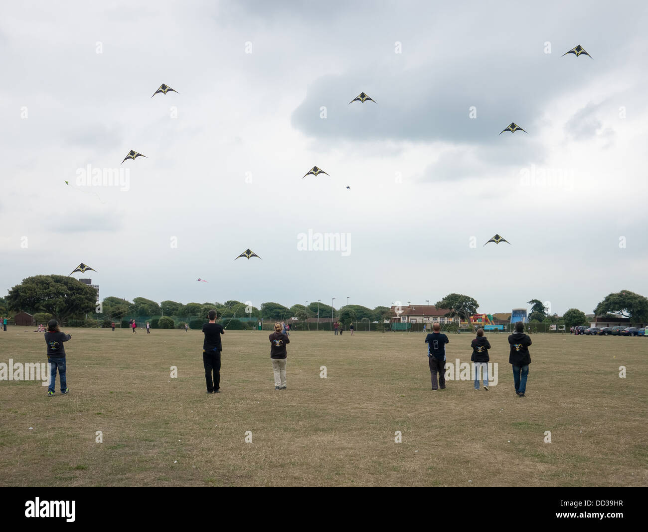 I membri di un kite team display stand in linea e volare i loro aquiloni in coordinamento Foto Stock
