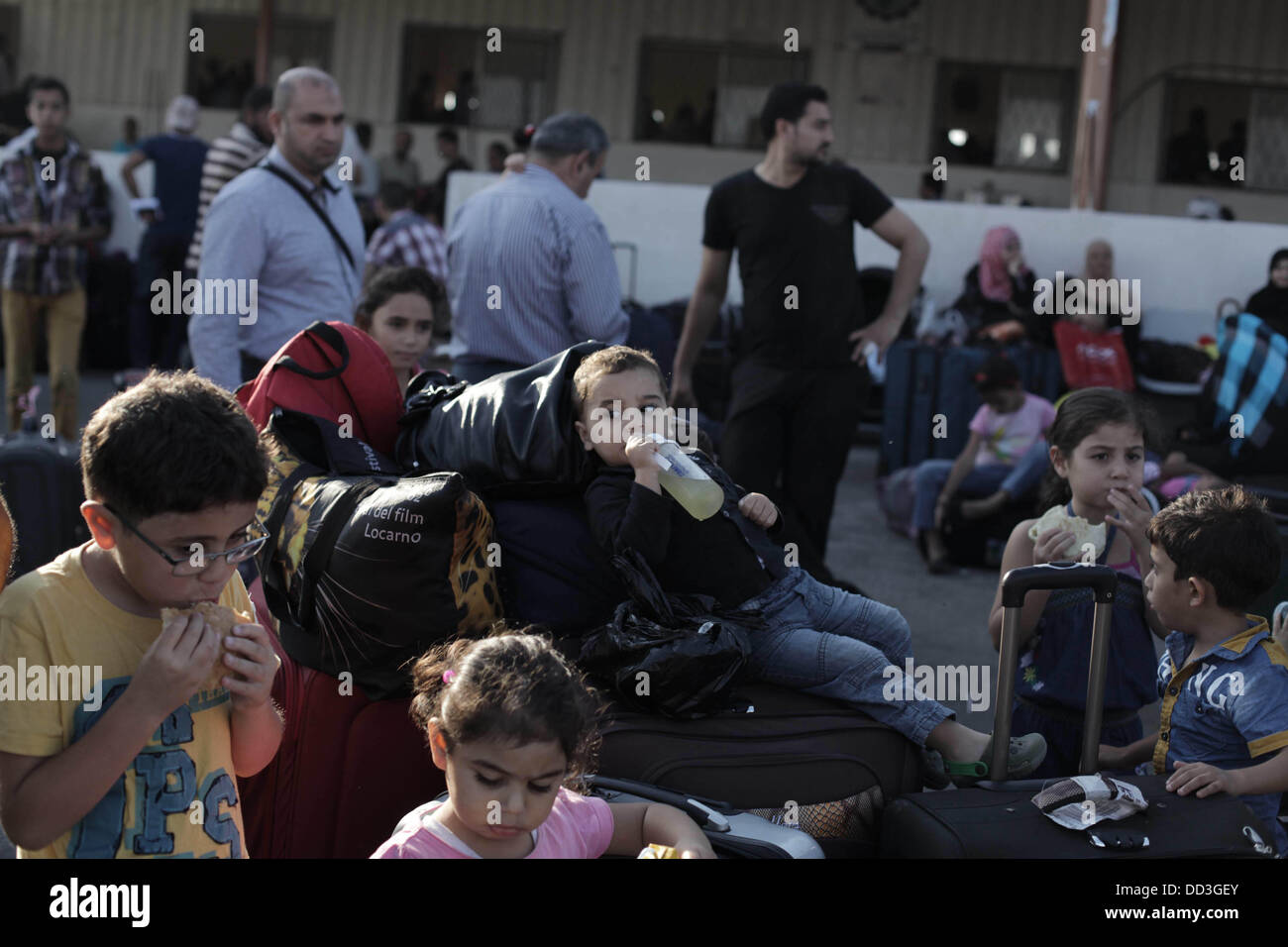 Rafah nella striscia di Gaza, Territori palestinesi. 25 Ago, 2013. Bambini palestinesi consumare cibi e bevande, in attesa di attraversare in Egitto al valico di Rafah tra Egitto meridionale e la striscia di Gaza il 25 agosto 2013. L'Egitto ha riaperto la sua frontiera con la striscia di Gaza il sabato dopo quattro giorni di chiusura, a filamento consentendo ai passeggeri di attraversare in e fuori del territorio palestinese. Migliaia di palestinesi, compresi gli studenti e pazienti che cercano un trattamento medico, non erano state in grado di viaggiare in Egitto dal Rafah varcare il confine era chiuso e centinaia che vogliono tornare a casa era stata s Foto Stock