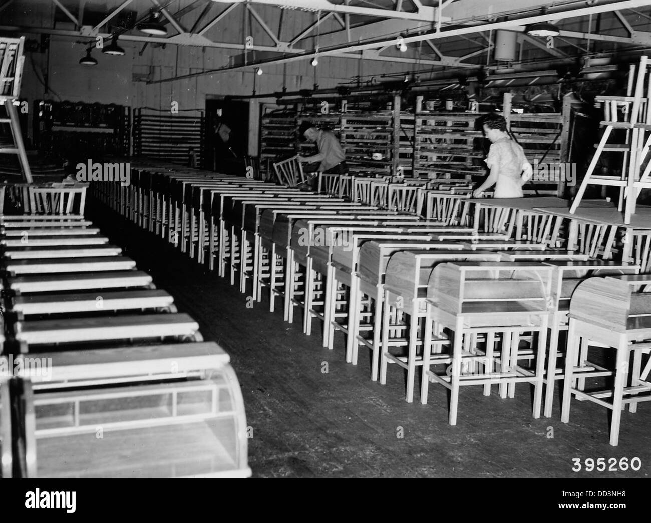 Una fotografia dei lavoratori che ispezionano le scrivanie e i seggioloni per bambini, probabilmente in un ambiente di fabbrica in cui tali oggetti sono fabbricati per scuole o case. Foto Stock