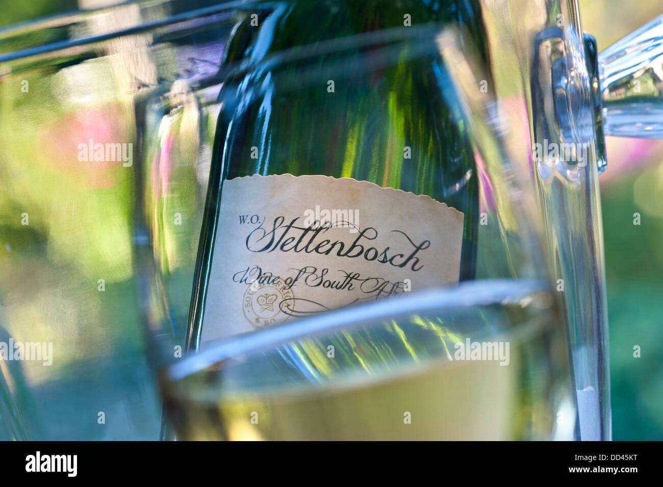 Closeup bicchiere da vino con Stellenbosch Sud Africa di bottiglie di vino e lo scambiatore di calore dietro nel soleggiato giardino alfresco situazione Foto Stock