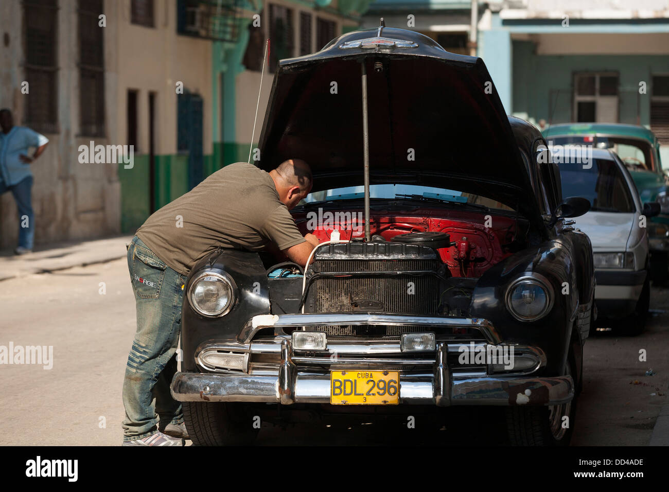 Un meccanico funziona sotto il cofano o il cofano del motore di un classico americano auto che è rotto per le strade di La Habana, Cuba Foto Stock