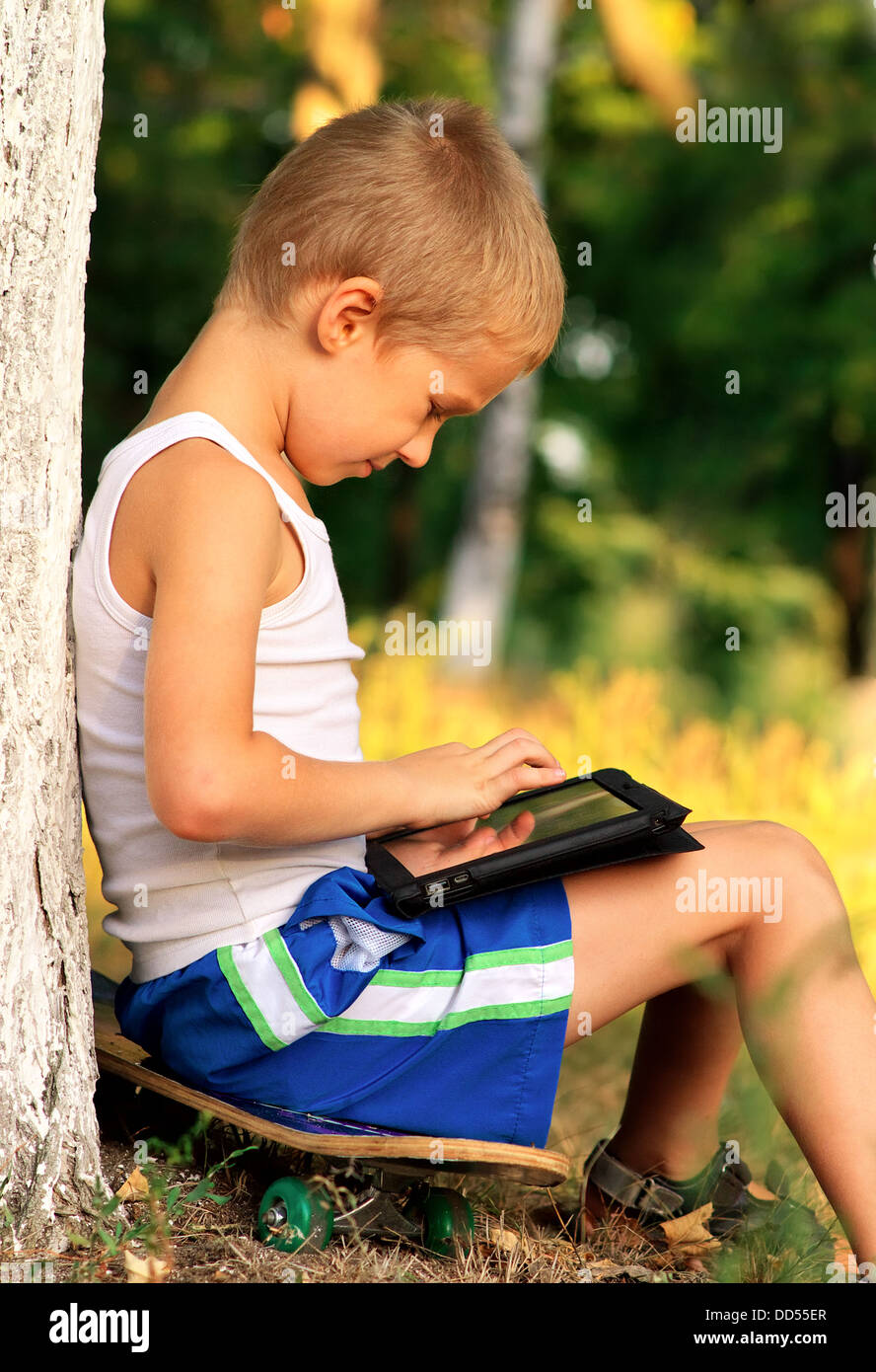 Ragazzo bambino che gioca con i Tablet PC esterno con foresta sul computer in background del gioco il concetto di dipendenza Foto Stock