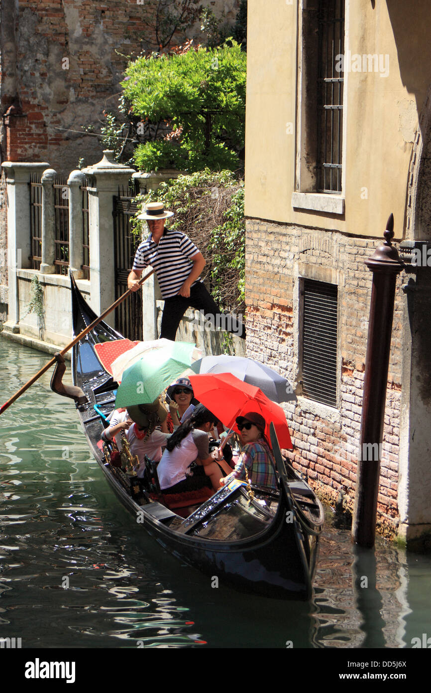 Asian gruppo turistico equitazione una gondola a Venezia. Ombrelloni in bandiera italiana di colori. Foto Stock