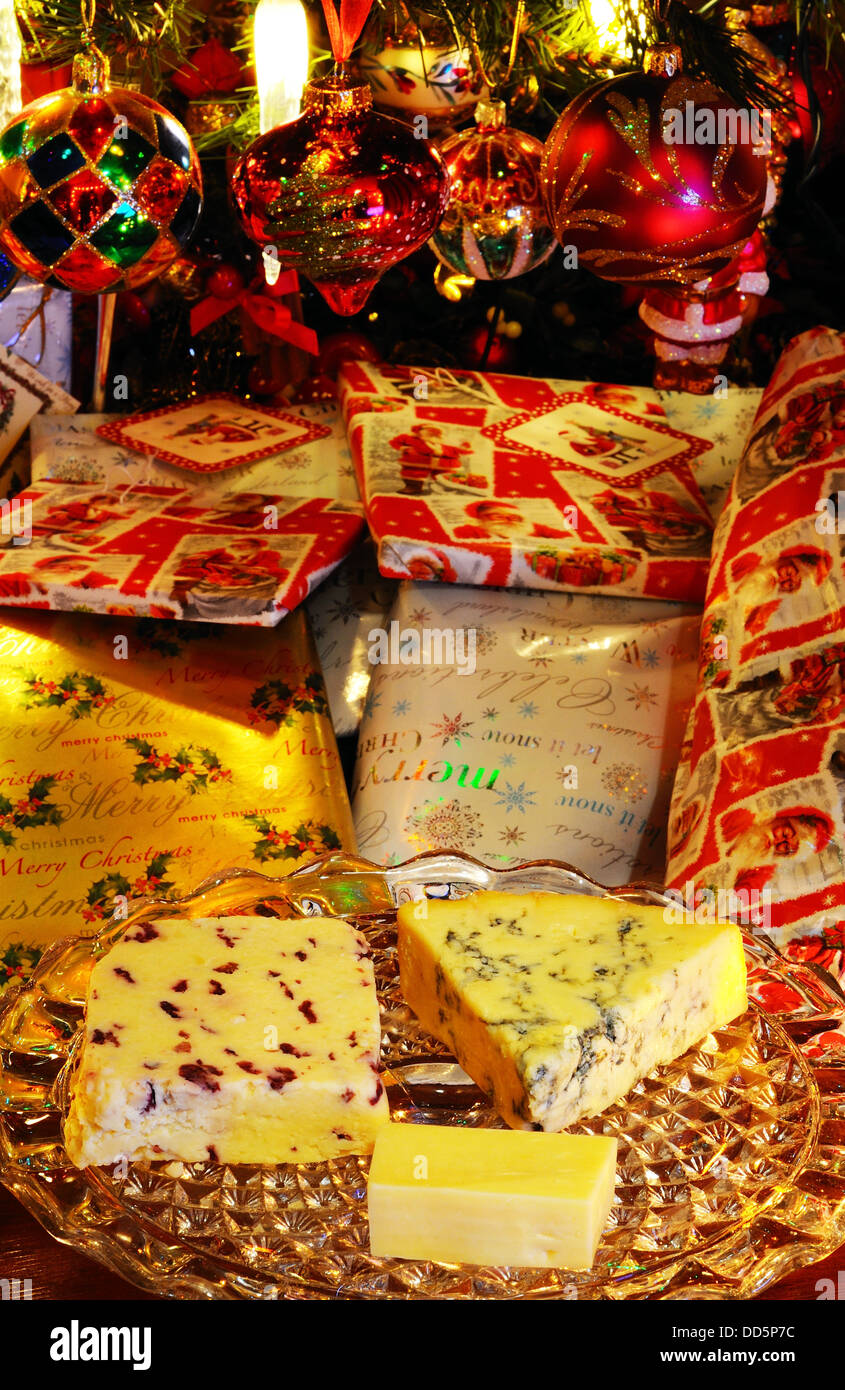 Blue Stilton, Wensleydale con mirtilli rossi e i formaggi Cheddar su una piastra di vetro stand con i regali di Natale & tree verso la parte posteriore Foto Stock