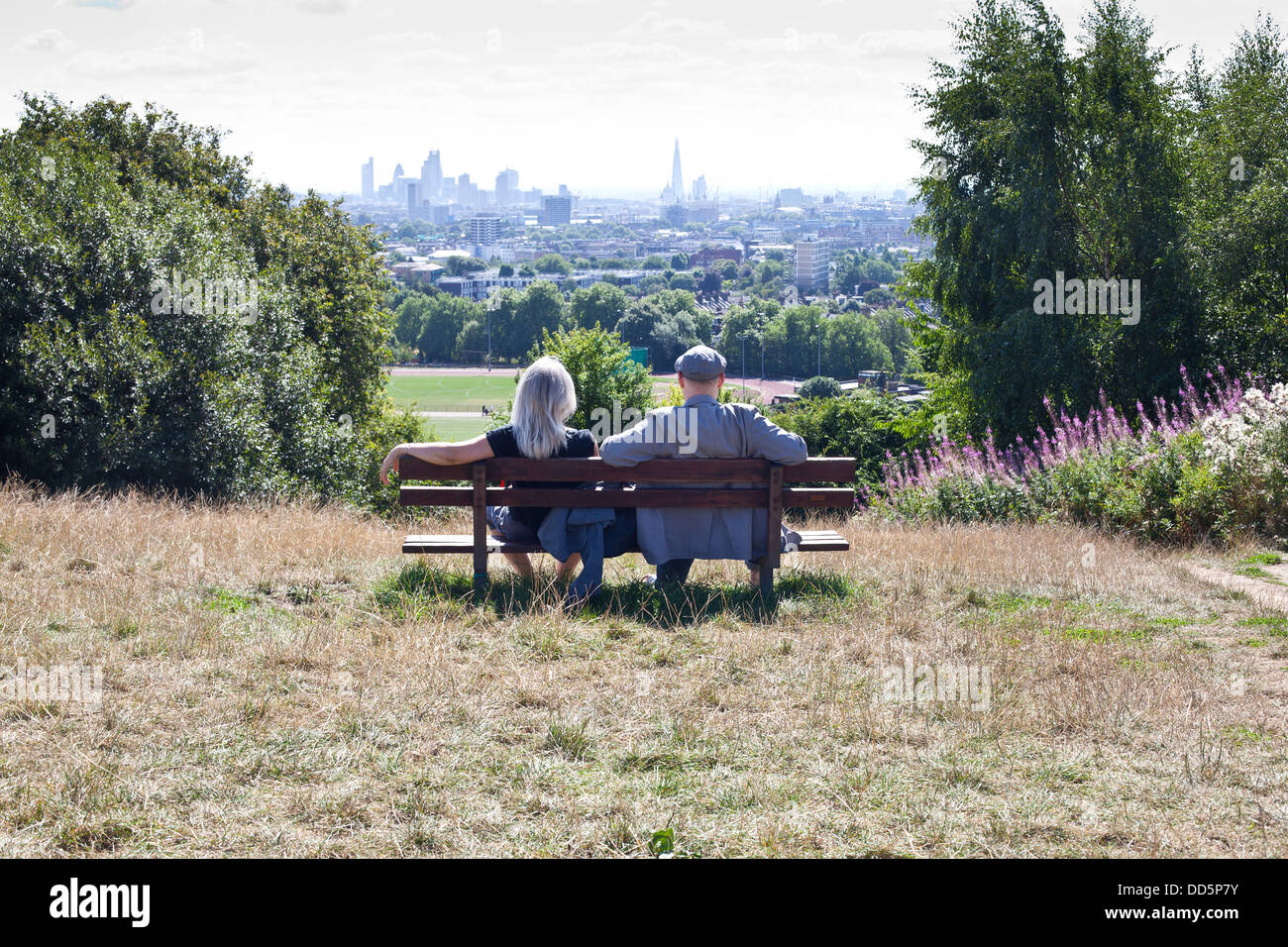 Giovane seduto su un banco di lavoro guardando lo skyline di Londra di Parliament Hill, Hampstead Heath Foto Stock
