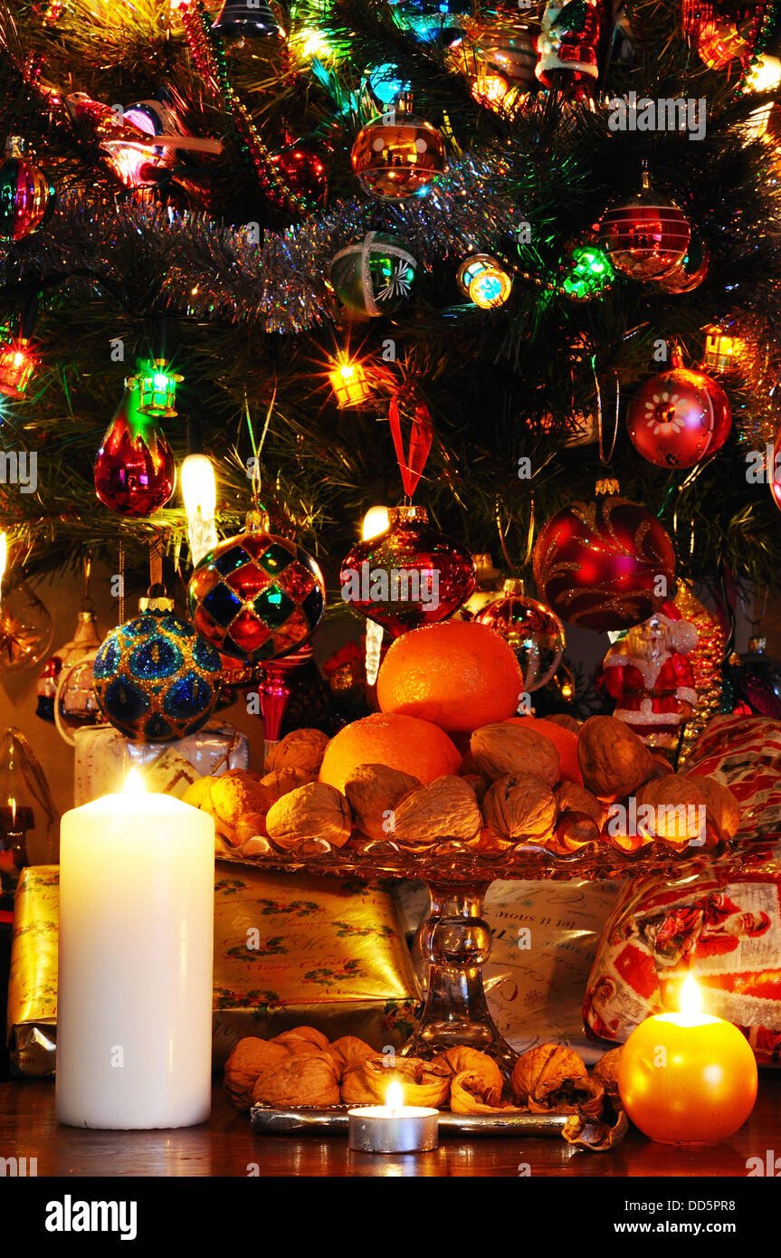 Lastra di vetro stand guarnita con noci, nocciole e mandarini arance con i regali di Natale sotto la struttura ad albero per la parte posteriore. Foto Stock