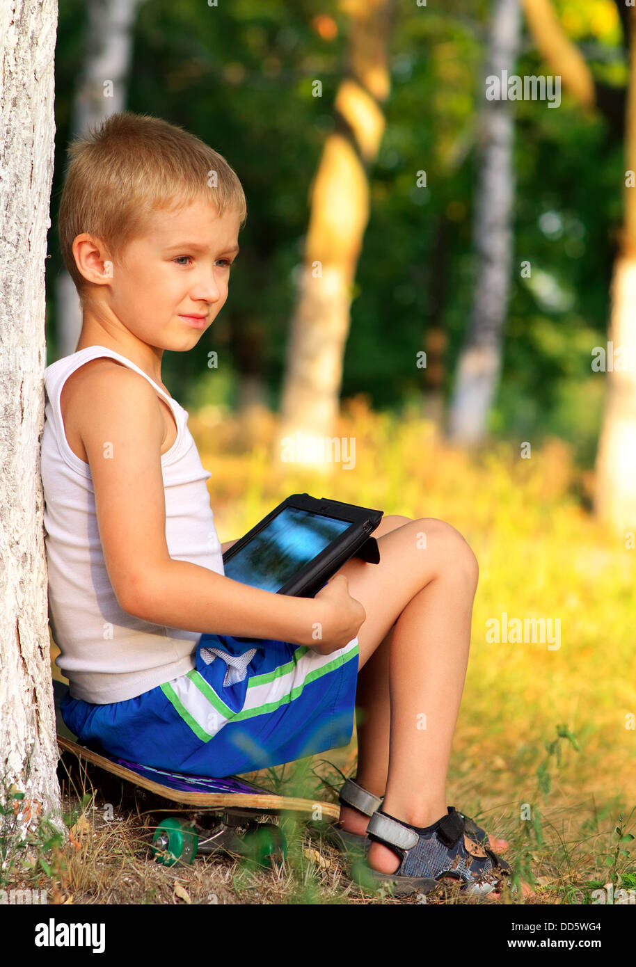 Ragazzo bambino che gioca con i Tablet PC esterno con foresta sul computer in background del gioco il concetto di dipendenza Foto Stock