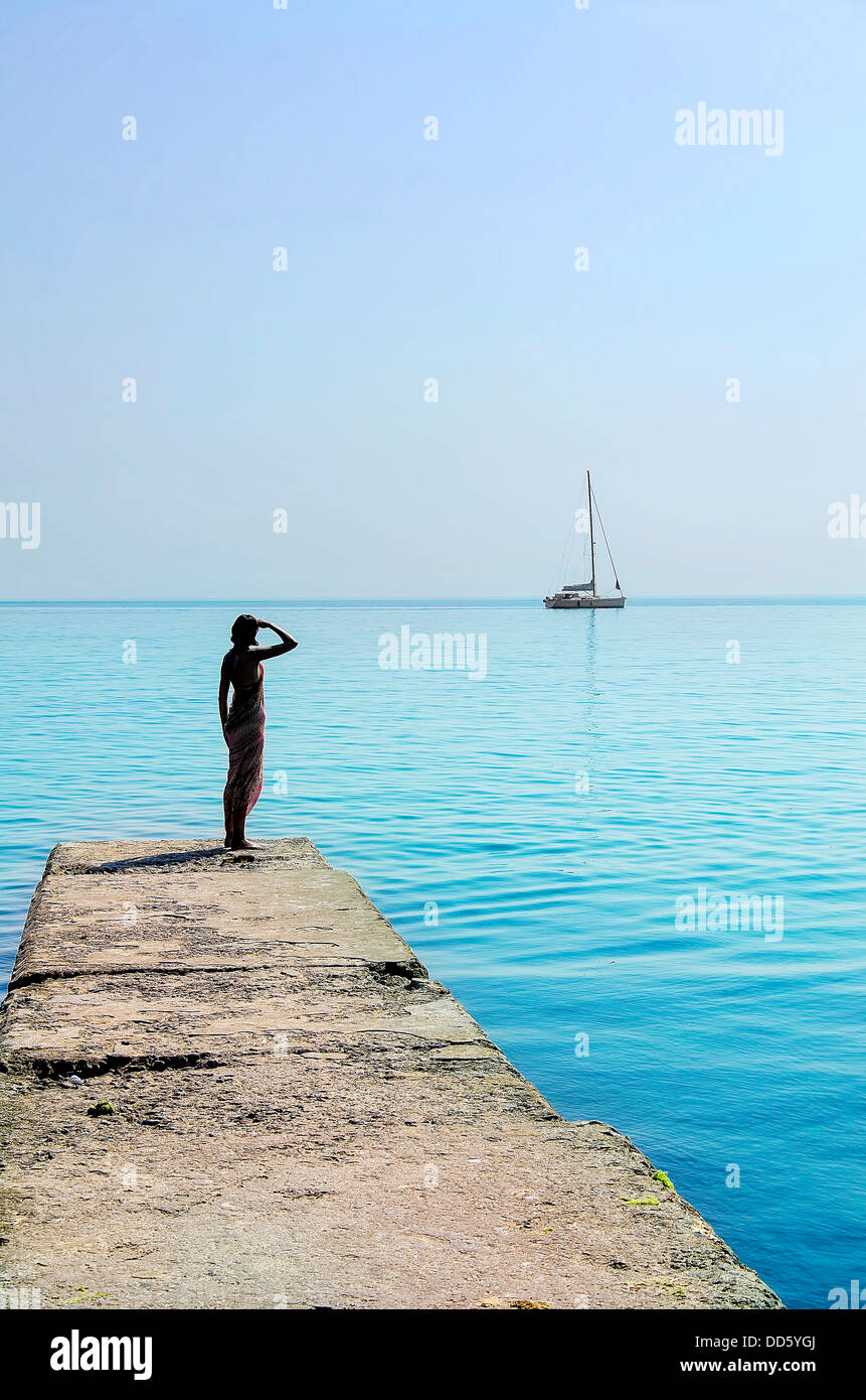 Donna in piedi su un molo di pietra guardando la barca Foto Stock