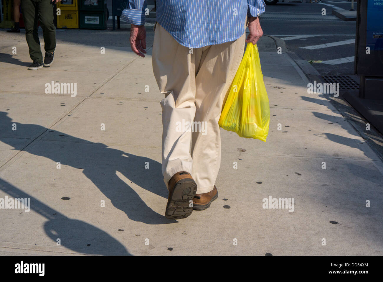 Una shopper lascia un supermercato con una busta di plastica tenendo la sua negozi di generi alimentari Foto Stock