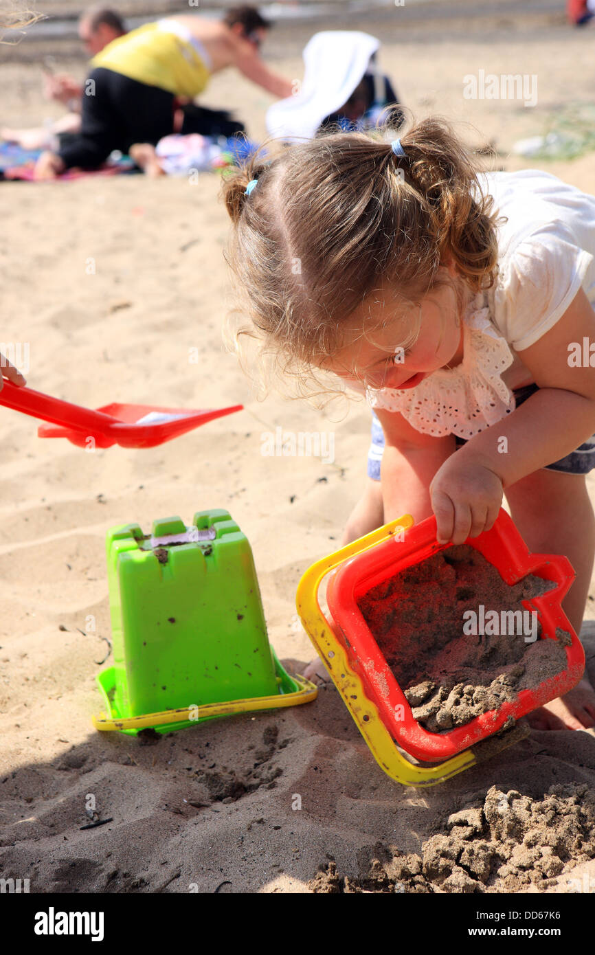 2 anno vecchia ragazza cercando di fare un castello di sabbia sulla spiaggia a Troon in Ayrshire in Scozia Foto Stock