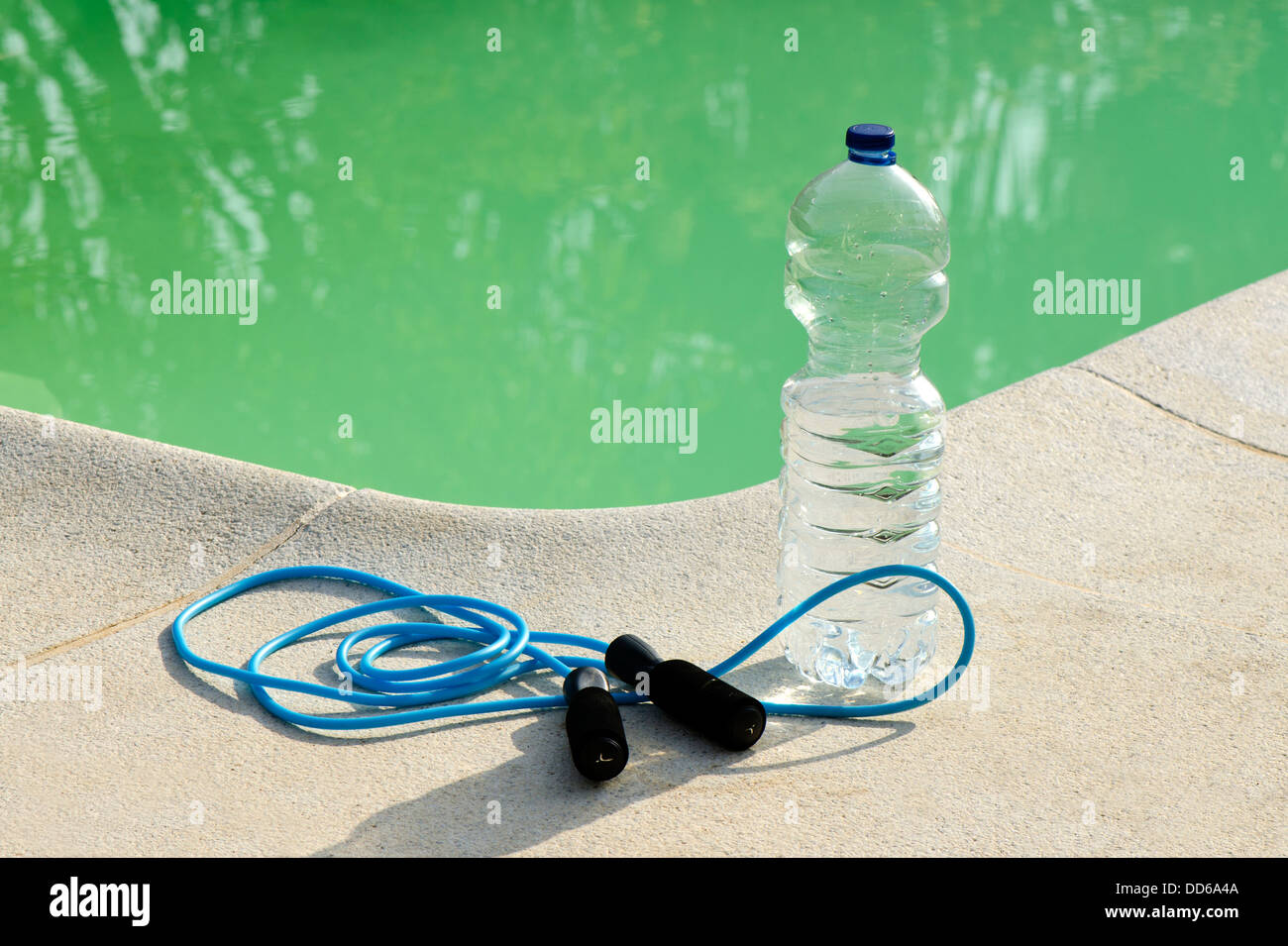 Corda da salto e una bottiglia di acqua vicino alla piscina Foto Stock