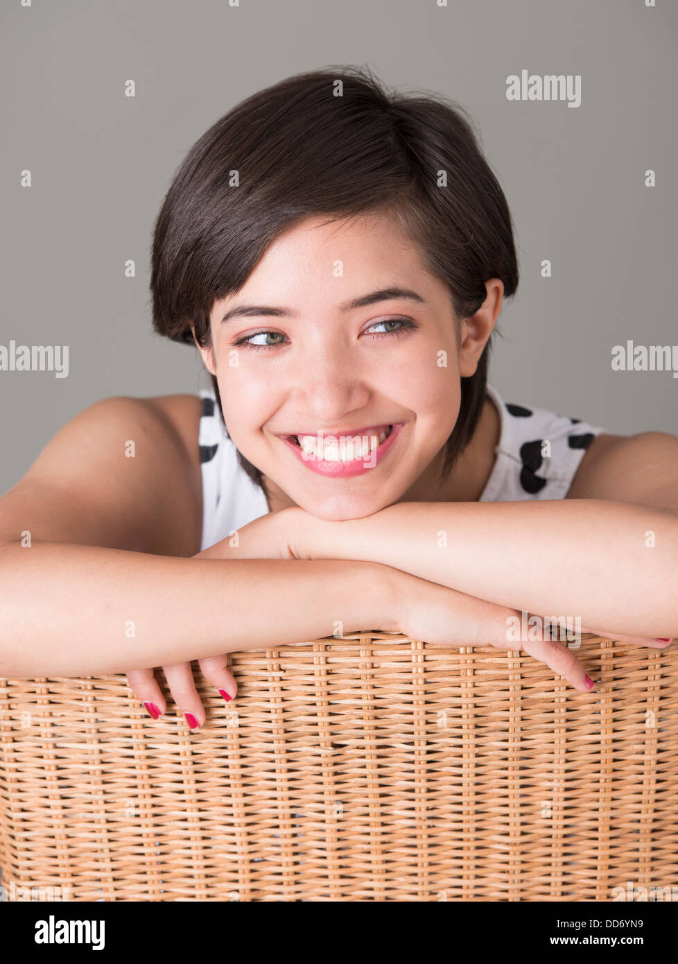 Fiducioso giovane donna seduta nella sedia di vimini che guarda lontano e sorridente Foto Stock