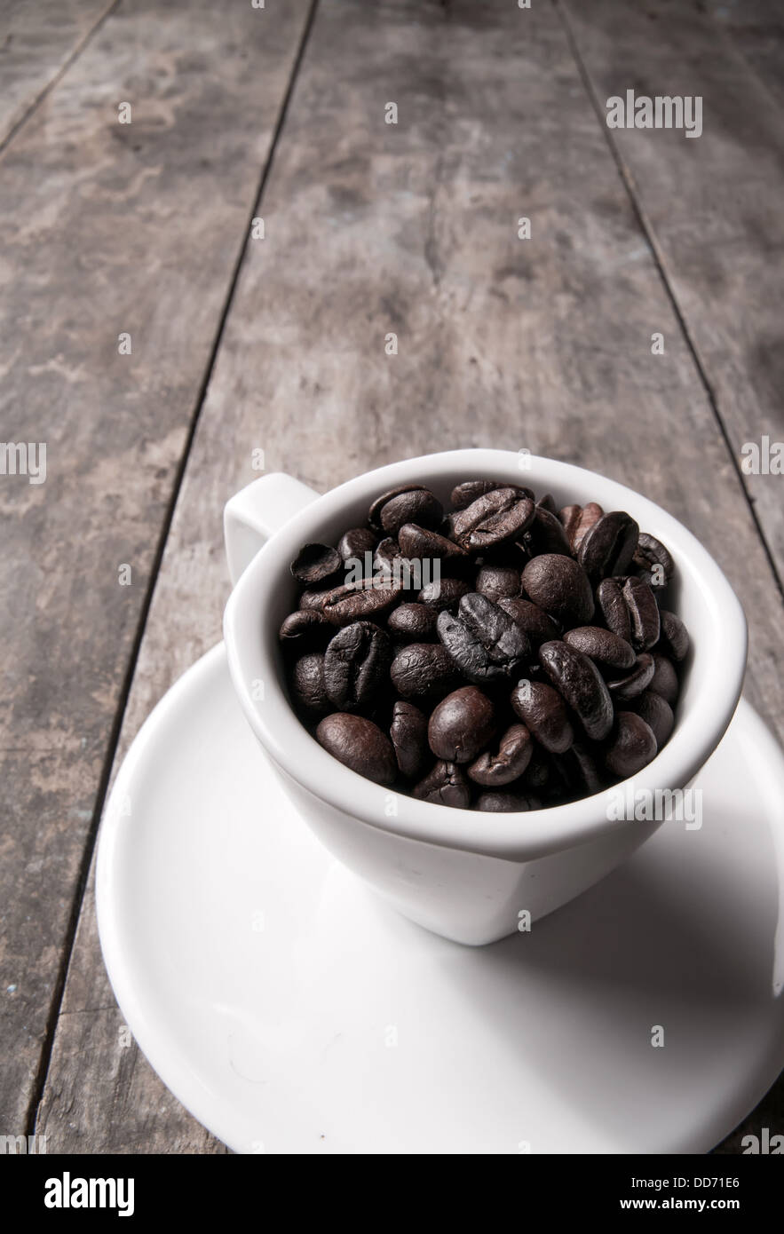 I chicchi di caffè in bianco tazza da caffè su sfondo di legno Foto Stock