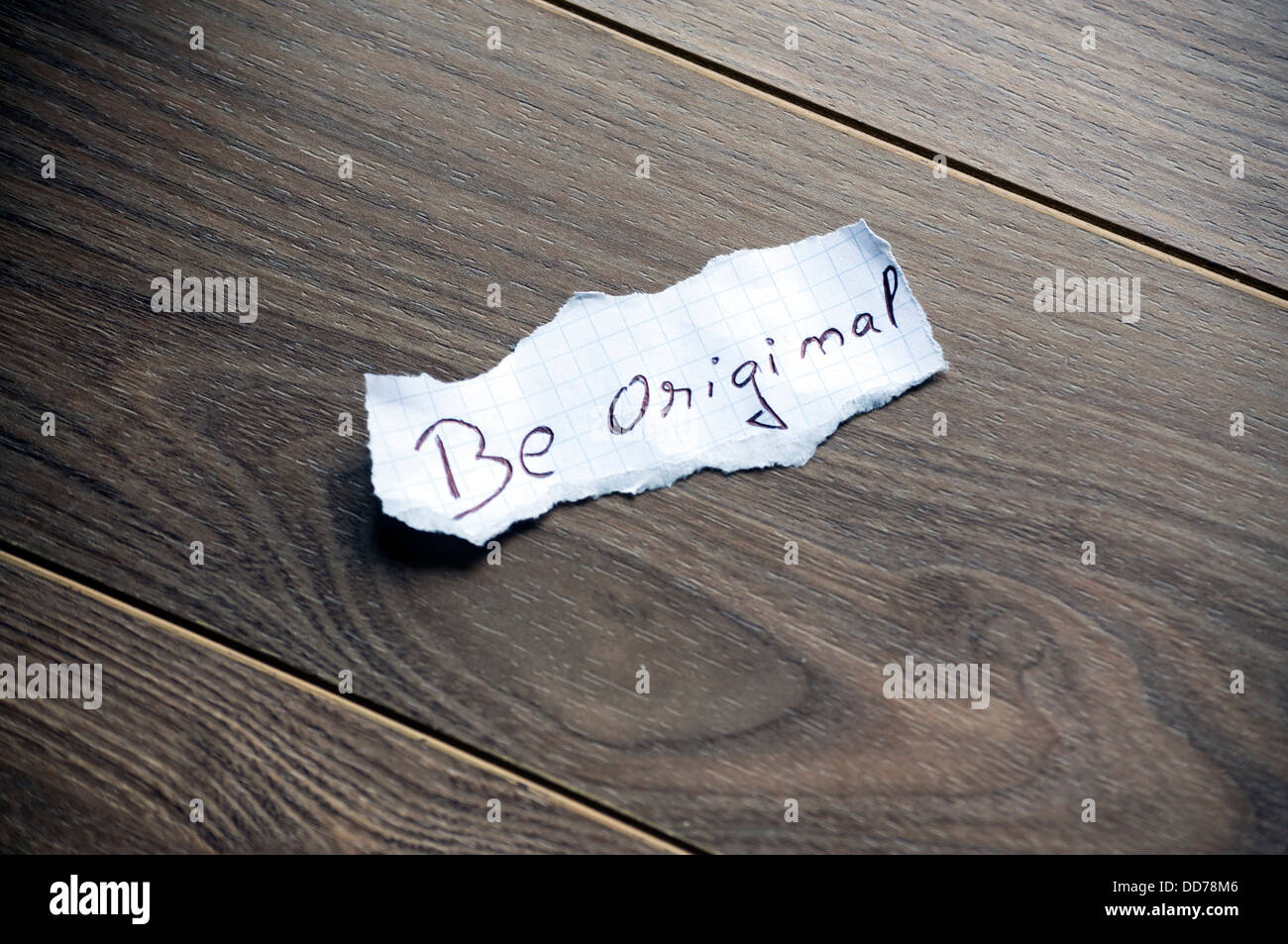 Essere originale scritto sul pezzo di carta su un sfondo di legno. Foto Stock
