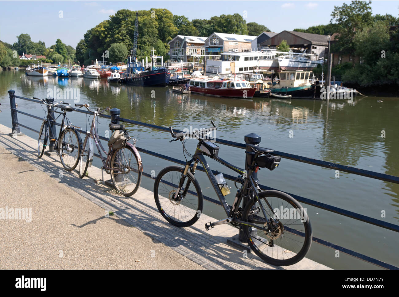 Tre biciclette bloccato a ringhiera accanto al fiume Tamigi a Twickenham, Inghilterra, il cantiere di anguilla isola a torta in background Foto Stock