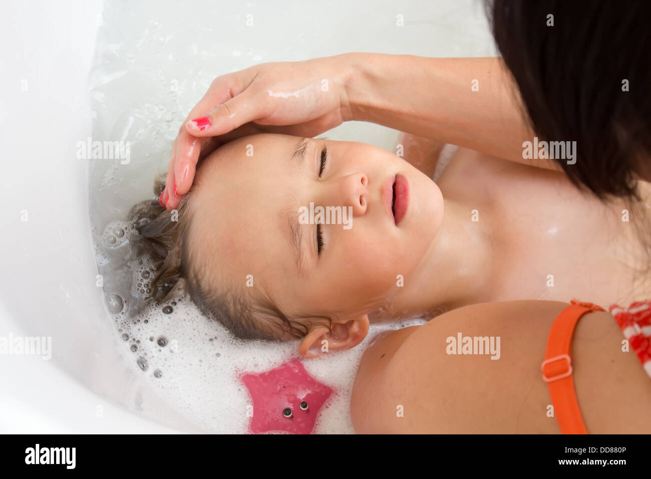 Una madre detiene il suo giovane figlio nelle sue braccia mentre ella lava i capelli con shampoo nella vasca da bagno Foto Stock