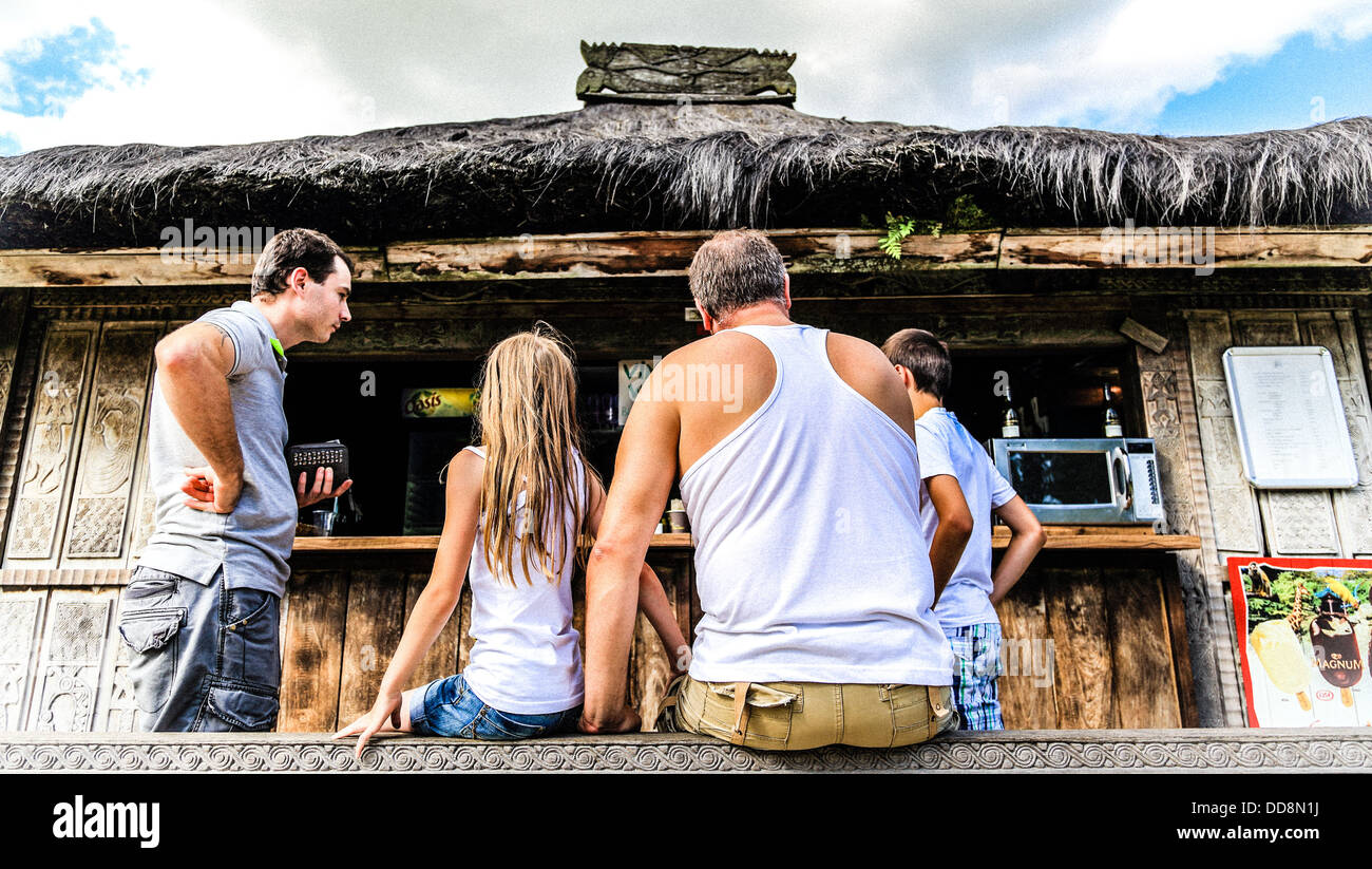 Una famiglia in attesa per un drink di fronte ad una piccola in legno esotico e casa. 4 bianco popolo europeo Foto Stock