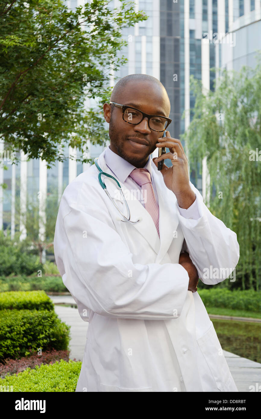 Medico nero parlando al cellulare nel parco urbano Foto Stock