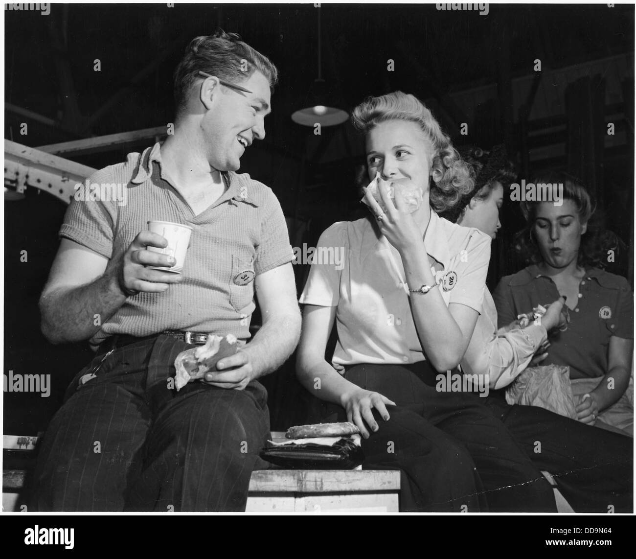 L'immagine cattura uomini e donne durante il turno di rotazione presso l'impianto aeronautico nordamericano di Inglewood, California, godendosi la pausa pranzo. Questa foto riflette l'ambiente di lavoro industriale e gli aspetti sociali della vita delle fabbriche durante la metà del XX secolo. Foto Stock