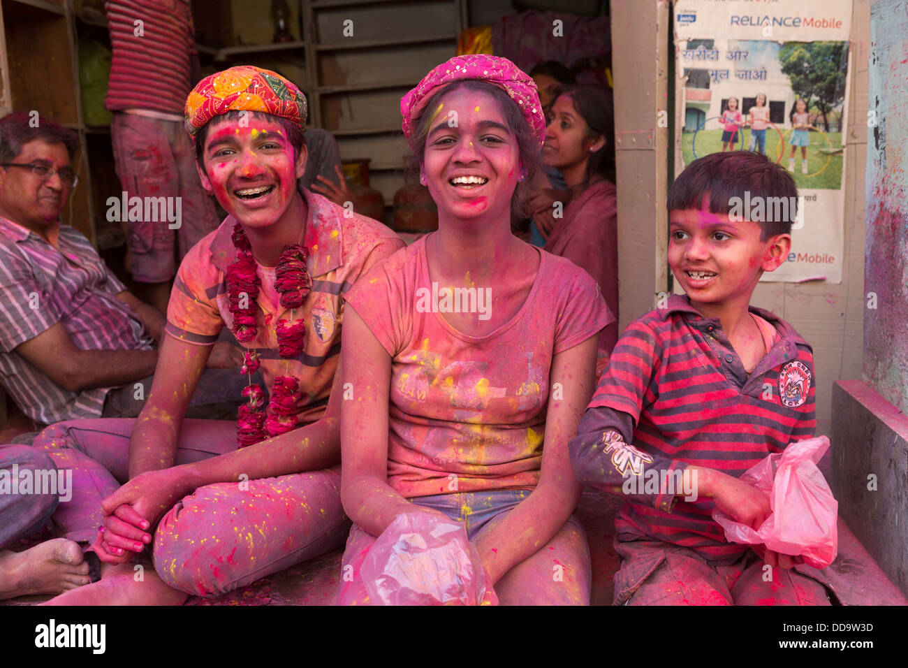Tre giovani divertirsi gettando polvere colorata a persone che camminano per la strada durante la celebrazione di Holi Foto Stock