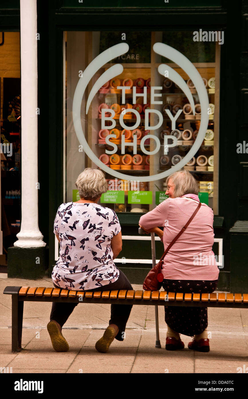 Due Anziani seduti su una panchina al di fuori del corpo Shop beauty store a Dundee, Regno Unito Foto Stock