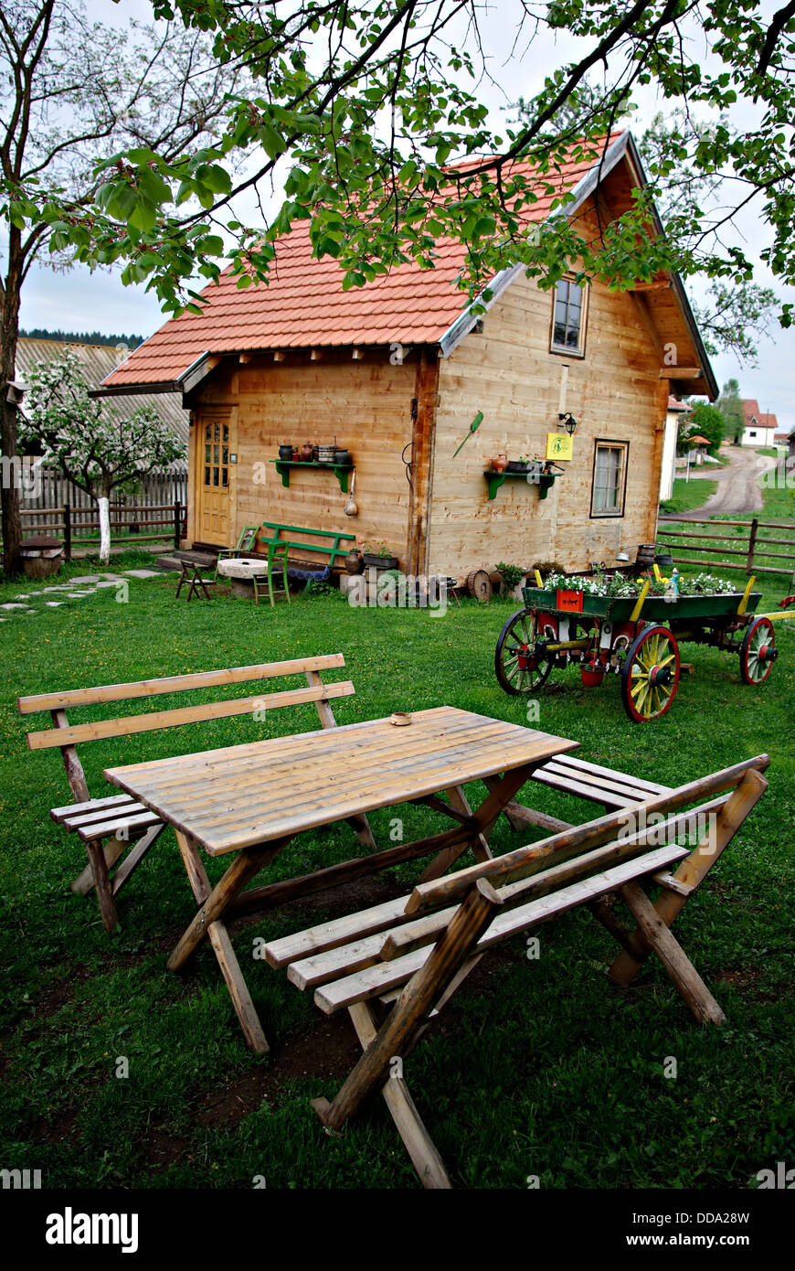 Antiche in legno log cabin, tavolo con panche e un vecchio vagone tirato da cavalli nel cortile agriturismo. Foto Stock