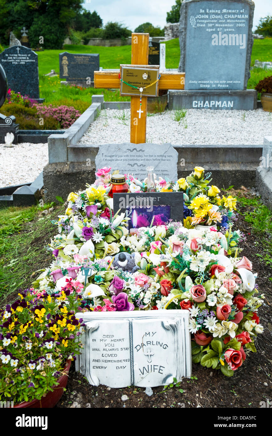 Una tomba in un irlandese cimitero rurale coperto con fiori di plastica Foto Stock