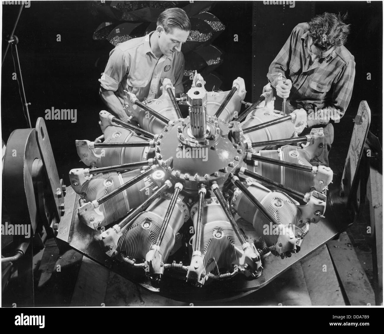 Due lavoratori stanno installando tubi di aspirazione a fila singola su un motore per aeroplani Pratt e Whitney in un grande stabilimento di produzione negli Stati Uniti orientali questa immagine cattura l'ingegneria industriale e l'assemblaggio nel settore dell'aviazione. Foto Stock