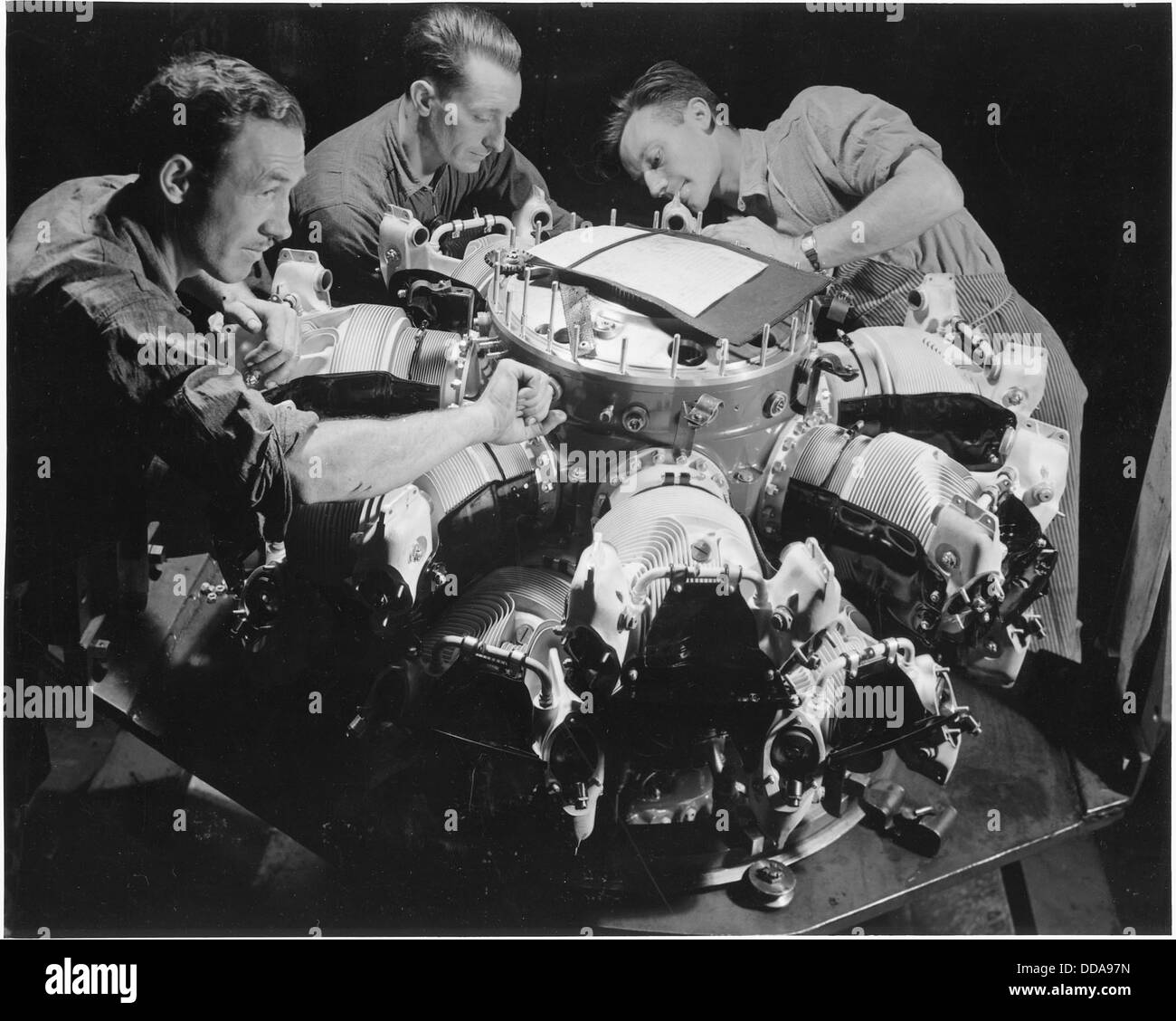 Questa fotografia mostra i lavoratori che installano cilindri su un motore per aeroplani Pratt e Whitney in un grande stabilimento di produzione. Il compito mette in evidenza la precisione tecnica necessaria per l’assemblaggio dei motori di aeromobili in un periodo chiave della storia dell’aviazione. Foto Stock