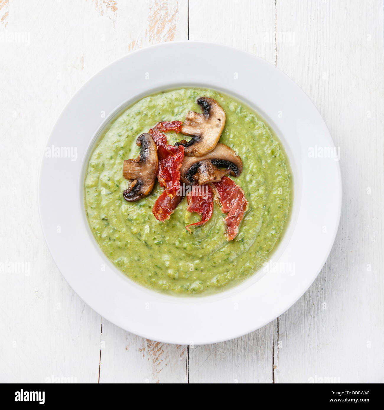 Verde zuppa di piselli in ciotola sul bianco sullo sfondo di legno Foto Stock