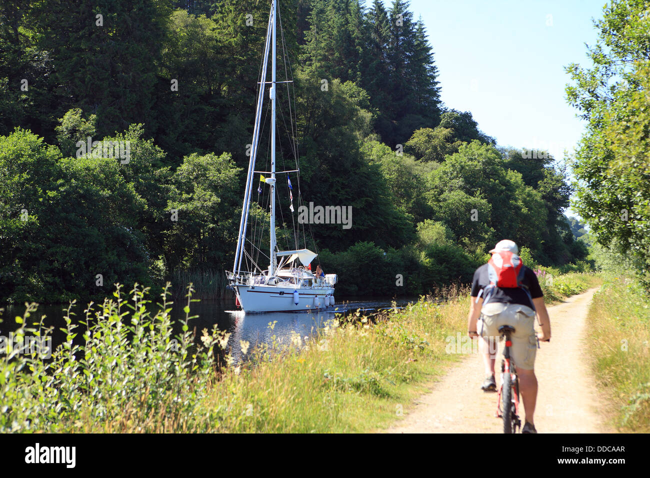 Ciclista sul Crinan Canal percorso ciclabile che passa una barca in canale in Argyll Scozia Scotland Foto Stock