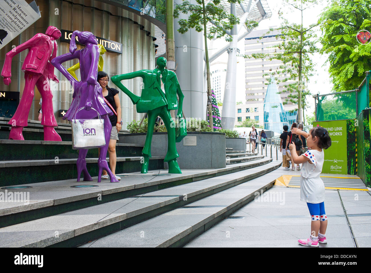 Un bambino prende una fotografia di sua madre al di fuori di ioni centro shopping con arte pubblica lavori in città asiatica stato di Singapore Foto Stock