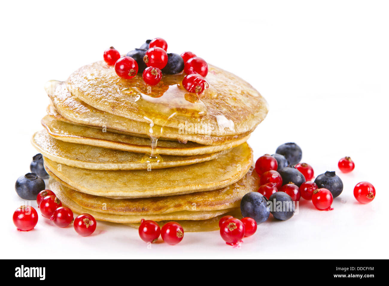 Piccoli pancake e rabboccato con miele, ribes rosso e mirtilli neri su sfondo bianco Foto Stock