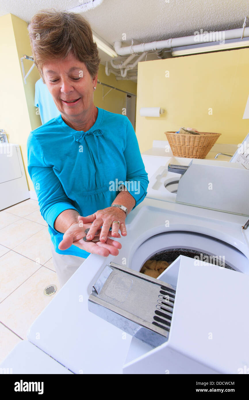 Senior donna contando il cambiamento per una lavatrice commerciale in una sala lavanderia Foto Stock
