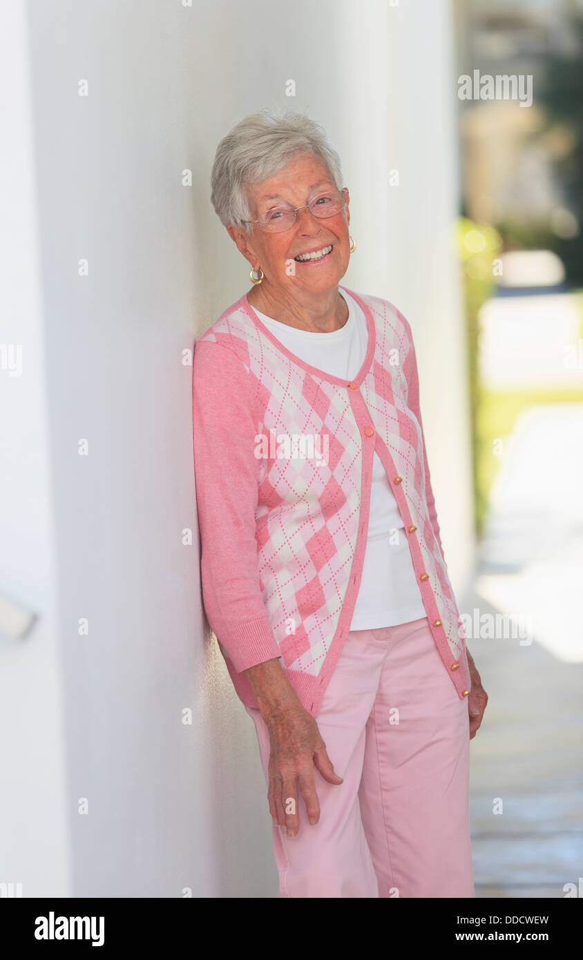 Senior donna sorridente appoggiato contro una parete Foto Stock