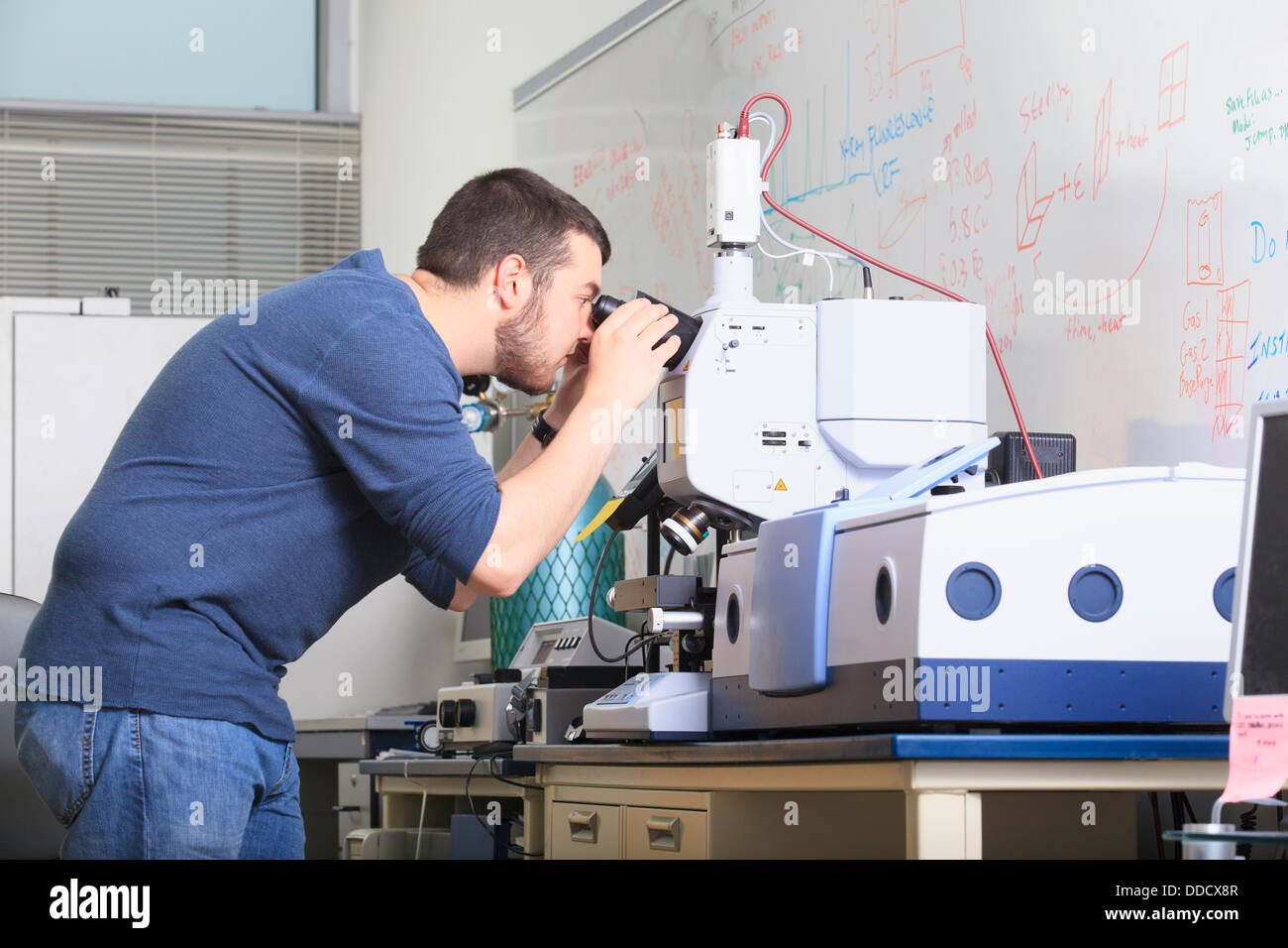 Studente di ingegneria guardando attraverso il microscopio ottico sulla chimica apparecchiature di analisi in un laboratorio Foto Stock