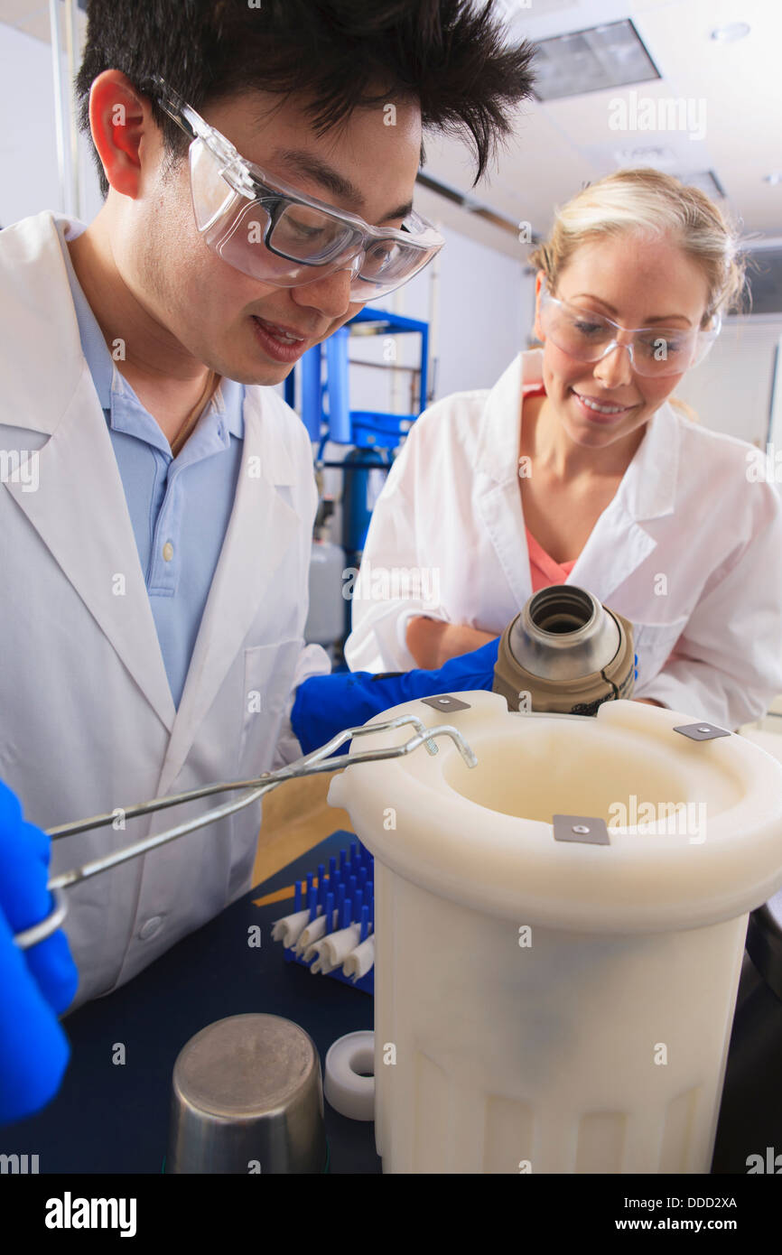 Gli studenti di ingegneria usando forcipi tenendo azoto liquido contenitore Dewar in acqua sala di elaborazione in un laboratorio Foto Stock
