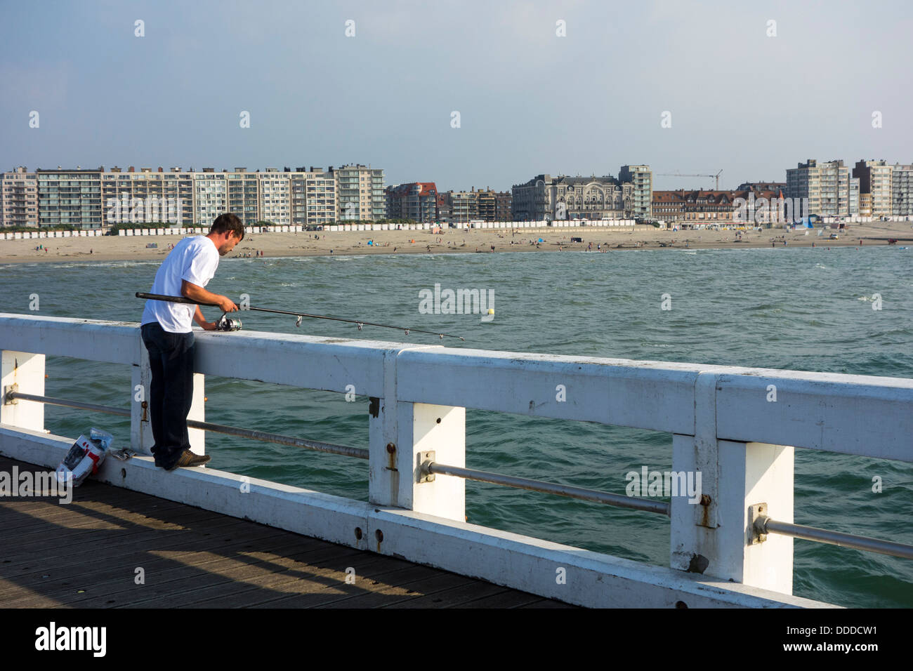 Il pescatore di pesca con canna da pesca dal molo lungo la costa del Mare del Nord a Nieuwpoort / Nieuport, Belgio Foto Stock