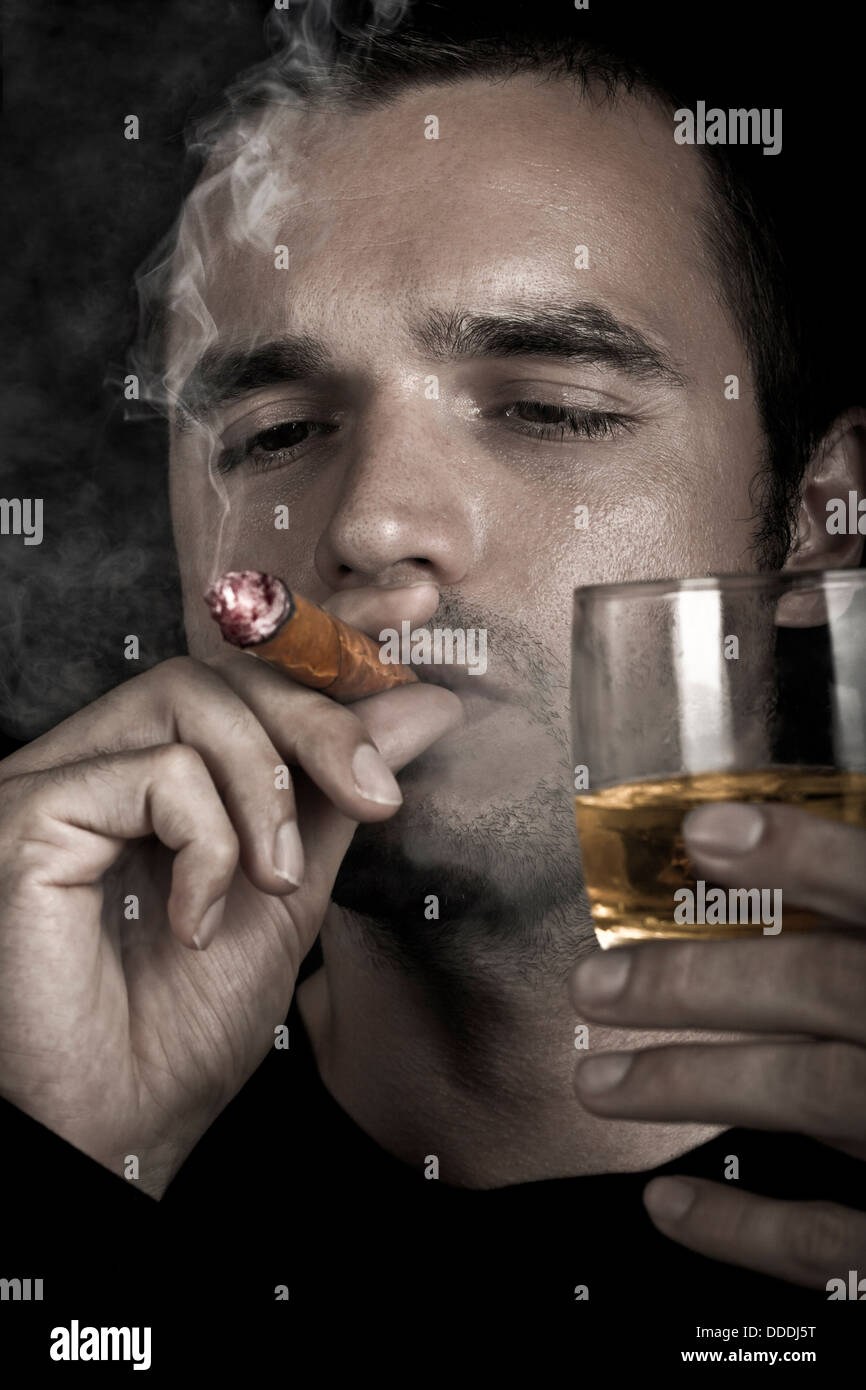 Dark drammatica foto di un uomo di fumare un buon sigaro e tenendo un bicchiere di whiskey. Foto Stock
