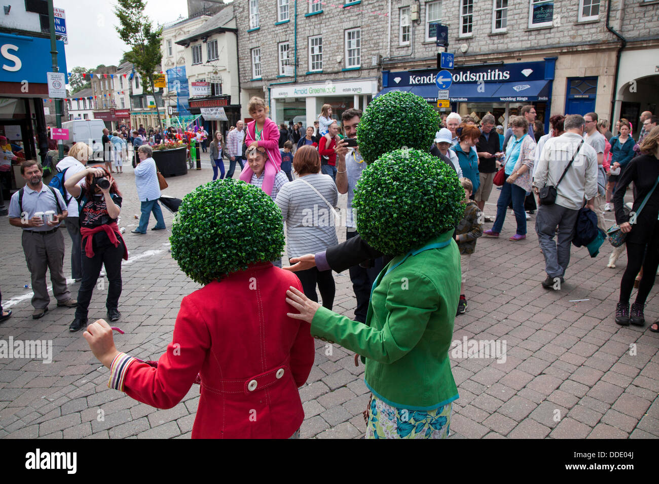 Testa rotonda, circolare, verde, parrucche artificiali frondosi, testa piantatrice indossata da artisti di strada a Kendal, Cumbria, Regno Unito. Agosto 2013. Mintfest, il Festival Internazionale di Street Arts di Kendal, le Potheads di Let's Circus, il negozio all'aperto Fat Face, un evento del weekend Lakes Alive nel Lake District che ha caratterizzato alcuni dei migliori artisti di tutto il mondo che hanno eseguito , danza contemporanea, circo, commedia, musica, gruppo eccentrico all'aperto per le strade. Foto Stock