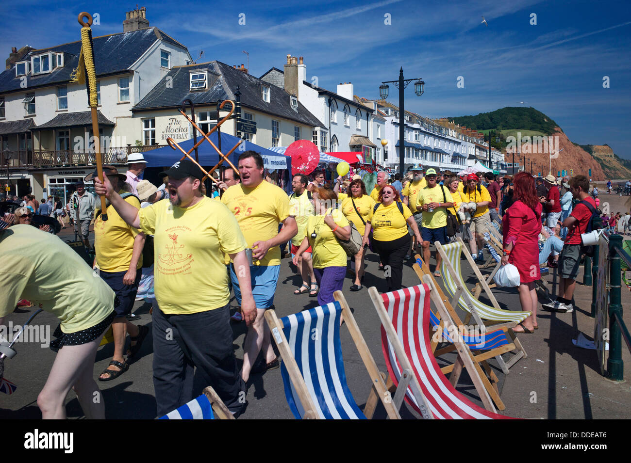 Un gruppo di cantanti marzo lungo l'esplanade nel corso del Festival di Sidmouth, Devon, Regno Unito Foto Stock
